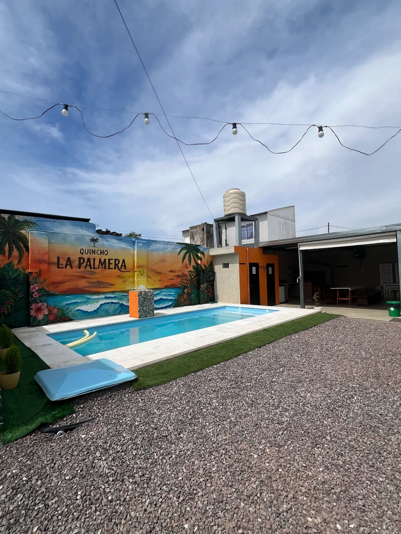 Vista general de la pileta, el mural tropical y el salón de Quincho La Palmera